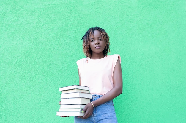 Piękna Afroamerykanka trzyma stos książek na zielonym tle Edukacja