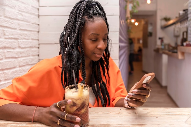 Piękna Afroamerykanka używająca telefonu komórkowego przy drinku