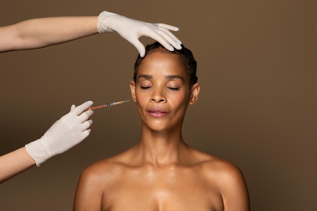 Piękna Afroamerykanka w średnim wieku, która otrzymuje zastrzyk na twarz w strefie kości policzkowych na stojąco
