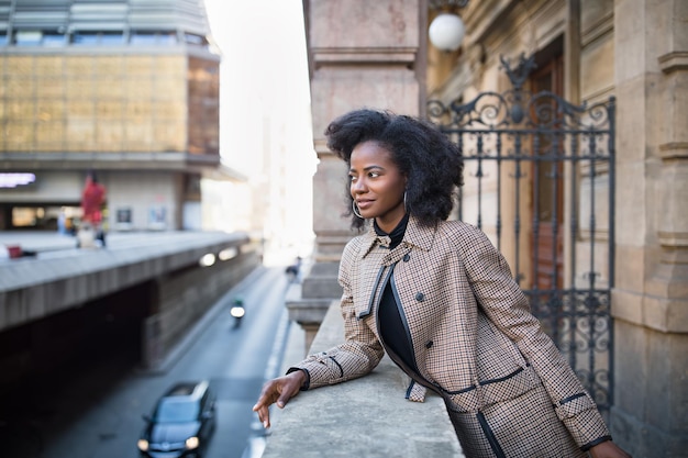 Piękna afroamerykańska młoda kobieta z afro i dużymi kolczykami w stylowym płaszczu miejskim życiu