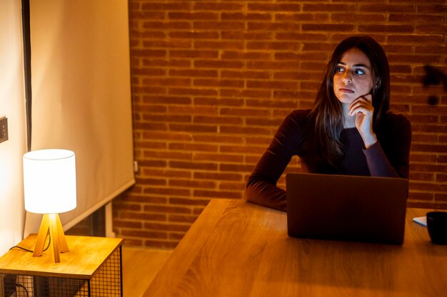 Piękna, autentyczna młoda kobieta siedząca przy stole w przytulnej kuchni i używająca laptopa w domu w nocy Kobieta uśmiechająca się i rozmawiająca w Internecie i mediach społecznościowych Robiąca badania online