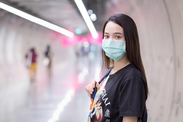 Piękna Azjatka nosi czarną koszulę i maseczkę medyczną, gdy wchodzi do tunelu metra