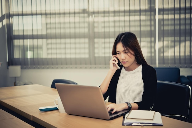 Piękna Azjatka pracująca wieczorem w biurze Pracownik z Tajlandii rozmawia przez telefon z szefem w firmie