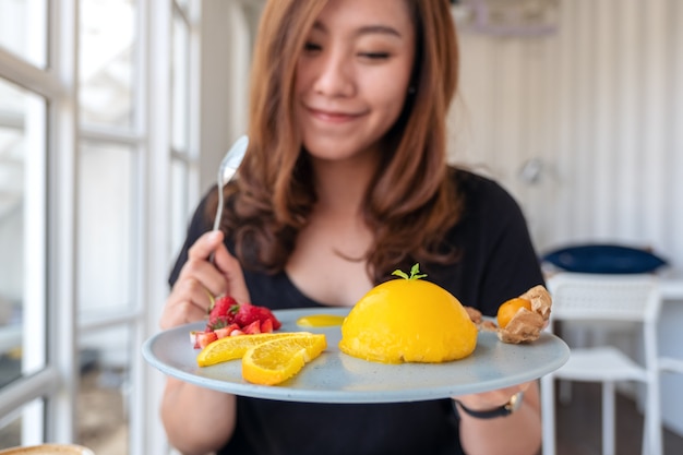 Piękna Azjatka Trzyma Talerz Pomarańczowego Ciasta Z Mieszanymi Owocami I łyżką W Kawiarni