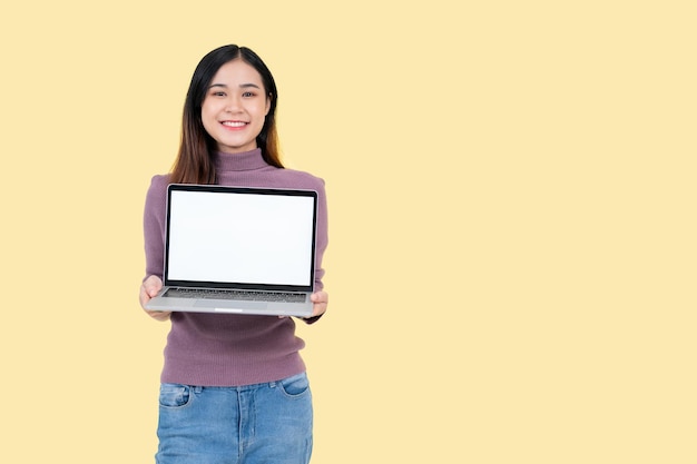 Piękna Azjatka trzymająca laptopa i stojąca na odizolowanym żółtym tle