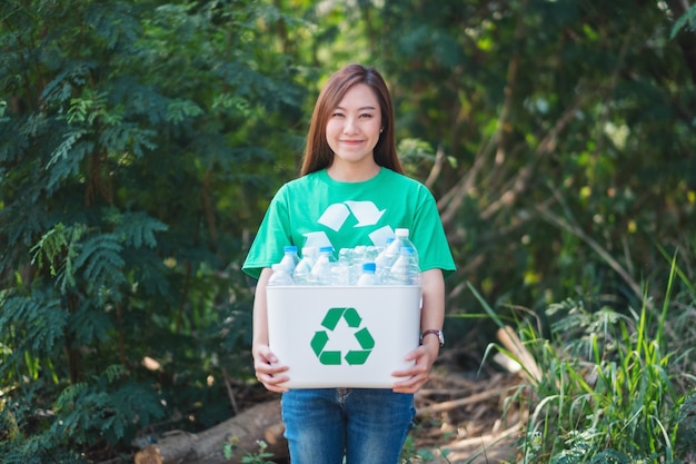 Piękna Azjatka zbierająca śmieci i trzymająca na zewnątrz kosz z plastikowymi butelkami