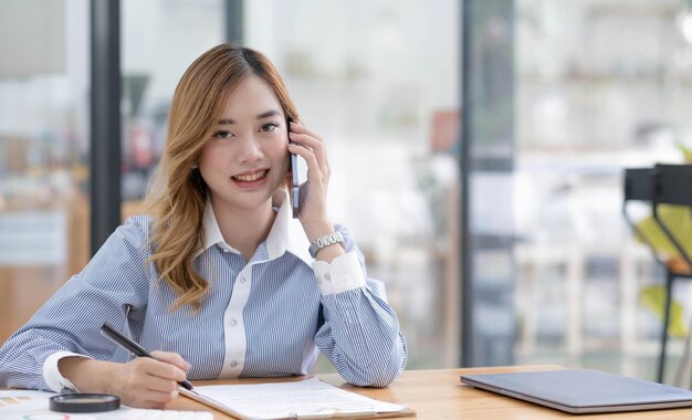 Piękna Azjatycka Bizneswoman Patrząca Na Kamerę W Biurze, Rozmawiając Przez Telefon Podczas Pracy W Biurze