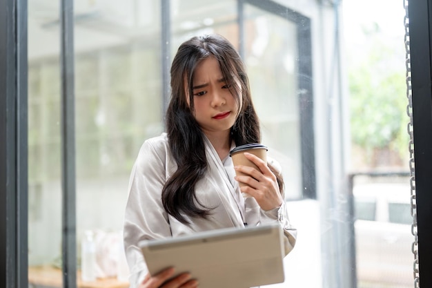 Piękna azjatycka bizneswoman patrzy na swój tablet z wątpliwą, poważną miną