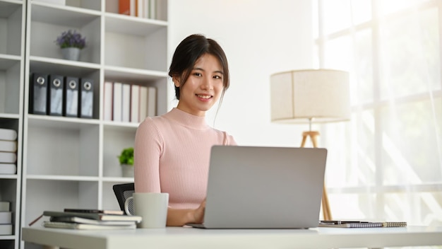 Piękna azjatycka bizneswoman siedzi przy biurku w swoim nowoczesnym prywatnym biurze