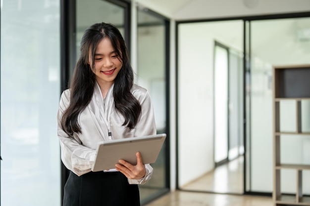 Piękna azjatycka bizneswoman używa cyfrowego tabletu w korytarzu biurowym