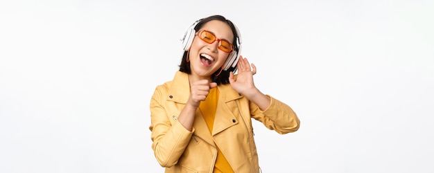 Piękna azjatycka dziewczyna śmiejąca się szczęśliwa muzyka słuchająca w słuchawkach stojących na białym tle
