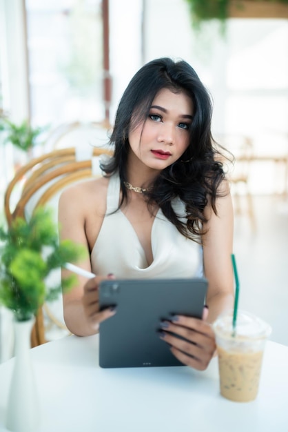 Piękna azjatycka freelancer Ludzie sukcesu biznes kobieta moda model w letniej białej sukience bez rękawów za pomocą swobodnej pracy z tabletem do przeglądania Internetu na czacie i blogowania w kawiarni