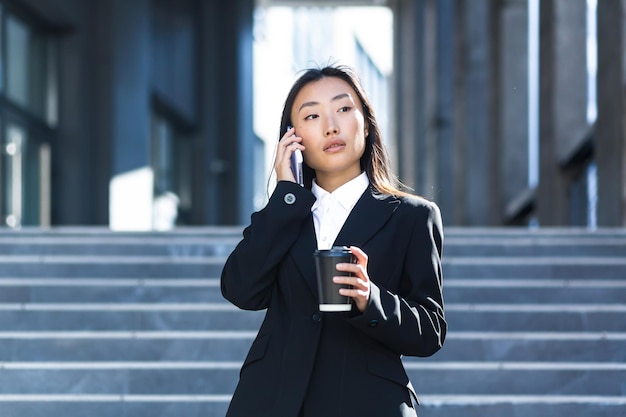 Piękna azjatycka kobieta bizneswoman spacerująca w pobliżu biura, rozmawiająca przez telefon w garniturze