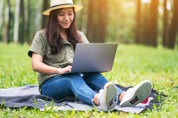 Piękna azjatycka kobieta pracująca i pisząca na klawiaturze laptopa siedząc w parku