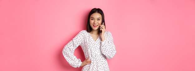 Piękna azjatycka kobieta rozmawiająca przez telefon komórkowy i uśmiechająca się stojąca nad różowymi półdupkami