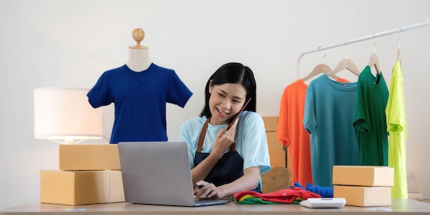 Piękna azjatycka kobieta sprzedawca online potwierdzający zamówienia od klienta przez telefon Rozpocznij małe firmy Właściciele MŚP Kobiety-przedsiębiorcy korzystają z laptopa w koncepcji homepack i dostawy