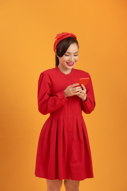 Piękna Azjatycka kobieta ubrana w czerwoną sukienkę i stojąca na pomarańczowym tle