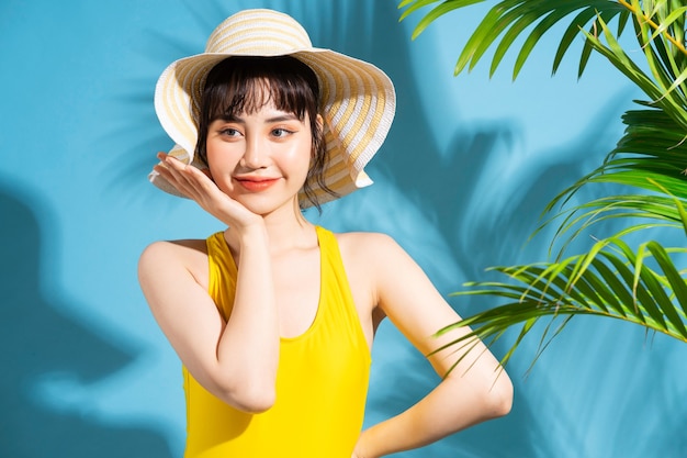 Piękna Azjatycka kobieta ubrana w żółty kombinezon na niebiesko z liśćmi palmowymi