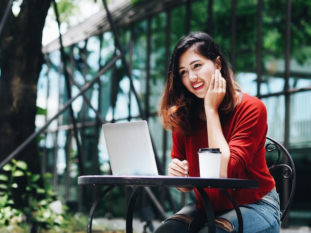 Piękna Azjatycka kobieta używa laptop przy kawiarnią
