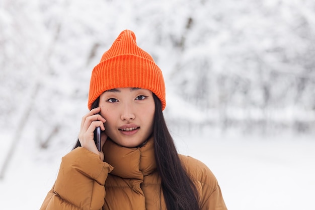 Piękna Azjatycka Kobieta W Ciepłych Ubraniach Rozmawia Przez Telefon W Parku W Zimowy śnieżny Dzień Na Spacerze