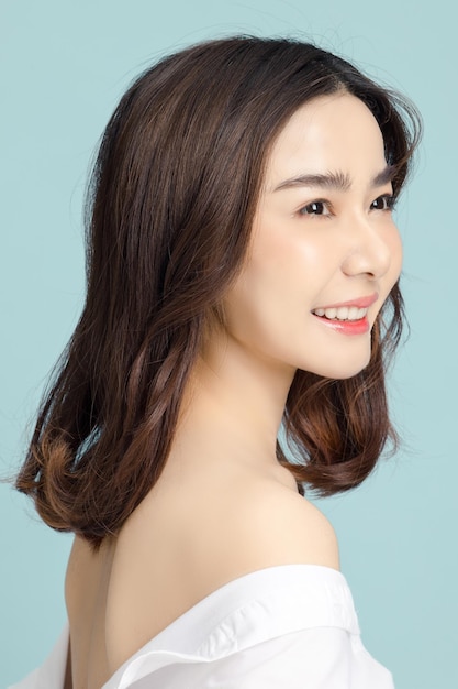 Piękna azjatycka modelka z krótkimi włosami z naturalnym makijażem i czystą świeżą skórą na niebieskim tle