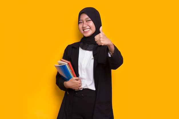 piękna azjatycka muzułmańska kobieta biznesu przytula książkę odizolowaną na żółtym tle