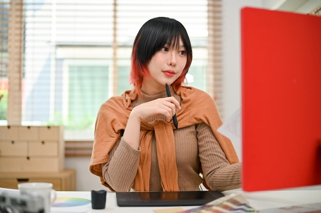 Piękna azjatycka projektantka graficzna pracująca nad swoim projektem na komputerze