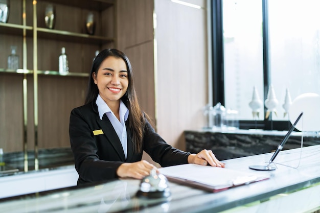 Piękna azjatycka recepcjonistka hotelowa w mundurach przy biurku w holu Przyjazny i mile widziany personel w recepcji hotelu