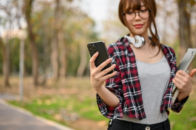 Piękna azjatycka studentka college'u używająca telefonu podczas spaceru w parku kampusu