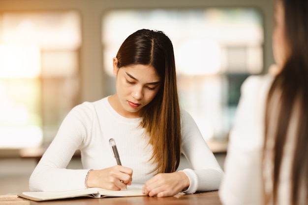 Piękna azjatycka studentka siedzi do egzaminu w klasie uniwersyteckiej studenci siedzą w rzędzie edukacja styl życia uczelnia uniwersytecka