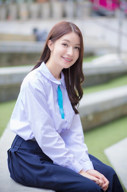 Piękna azjatycka uczennica liceum w szkolnym mundurku z szelkami na zębach