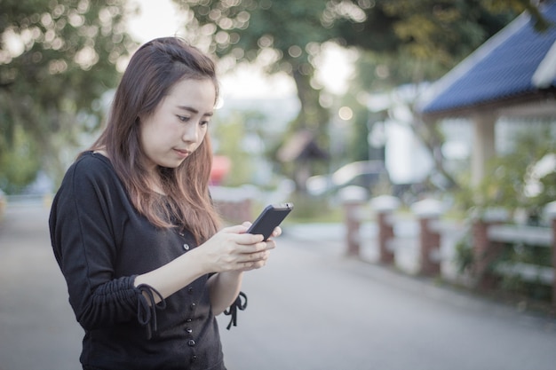 Piękna azjatykcia dziewczyna używa telefon komórkowego na drodze