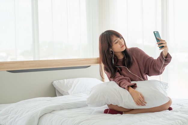 Piękna azjatykcia kobieta bawić się smartphone na łóżku