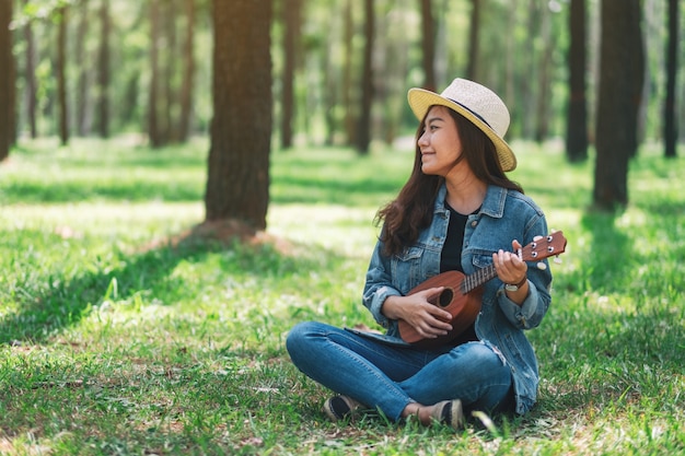 Piękna azjatykcia kobieta siedzi ukulele i bawić się w parku