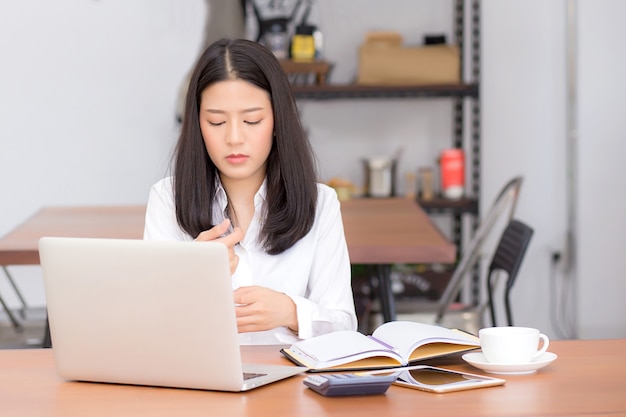 Piękna azjatykcia młoda kobieta pracuje online na laptopu obsiadaniu przy sklep z kawą.