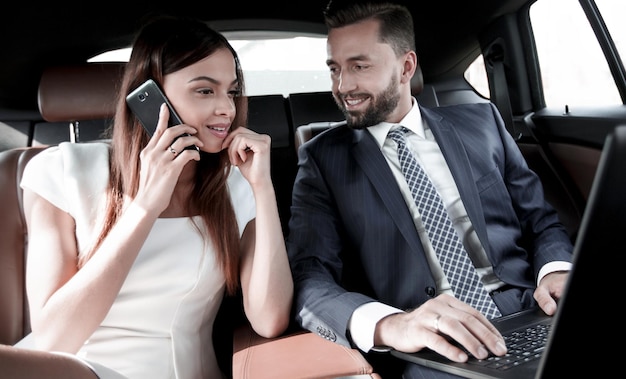 Piękna biznesowa kobieta rozmawia przez telefon komórkowy, siedząc na tylnym siedzeniu samochodu