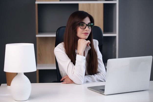 Piękna biznesowa kobieta używa laptopa i uśmiecha się podczas pracy w biurze.
