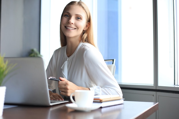 Piękna biznesowa kobieta w eleganckim stroju casual pracuje na laptopie w biurze