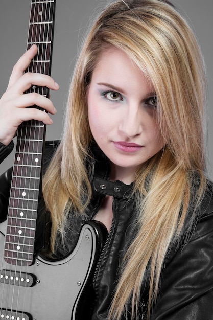 Piękna blond dziewczyna trzyma czarną gitarę elektryczną
