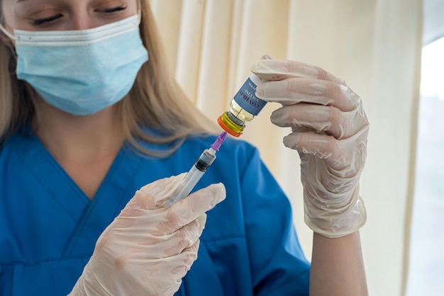 Piękna blond pielęgniarka w masce wybiera szczepionkę do strzykawki dla pacjenta
