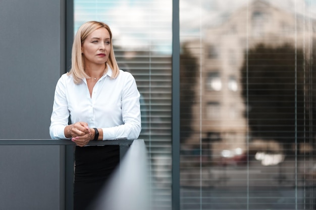 Zdjęcie piękna blond sekretarka stoi smutna w pobliżu okien biura