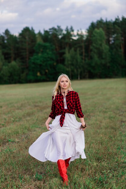 Zdjęcie piękna blondynka młoda kobieta w eleganckim kapeluszu w pobliżu starego drewnianego płotu i na polu z kucykami, panna młoda kraju