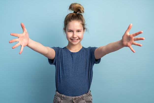 Piękna blondynka nastolatka girlwearing ubranie, patrząc w kamerę, uśmiechając się z otwartymi ramionami do uścisku