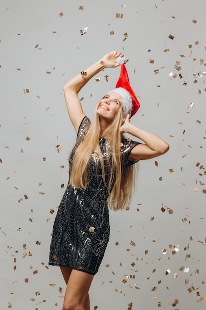 Piękna blondynka Santa dziewczyna tańczy pod błyszczącym konfetti koncepcja partii nowego roku