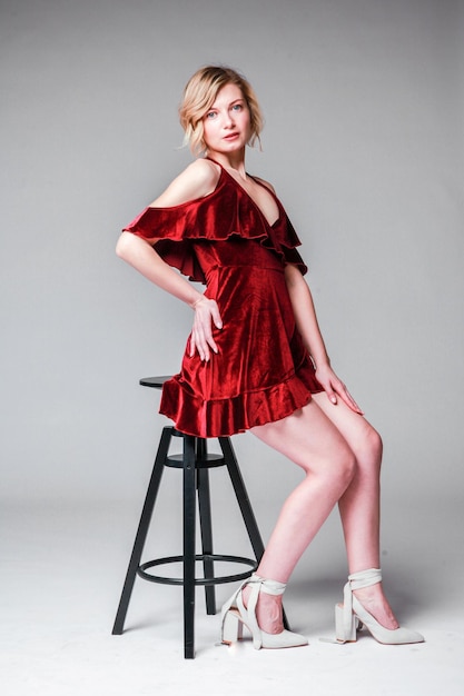 Piękna blondynka siedzi na krześle w czerwonej sukience w studio