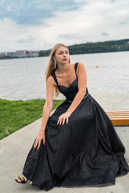 Piękna blondynka w czarnej eleganckiej modnej sukience stoi w pobliżu jeziora relaks i styl życia
