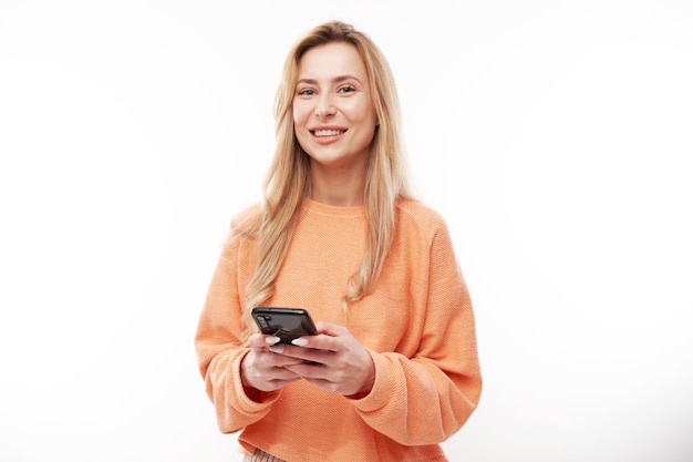 Piękna blondynka w swobodnym spojrzeniu na ekran smartfona i uśmiechy na białym tle studia
