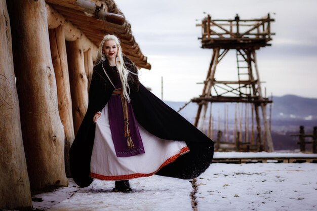 Piękna blondynka Wiking ubrana w czarną pelerynę na tle zamku