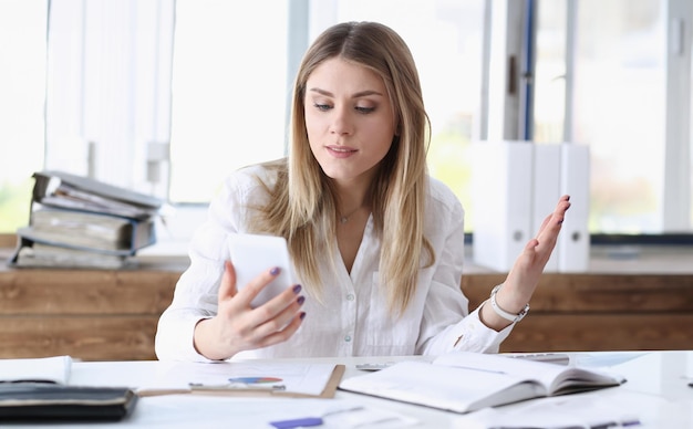 Piękna blondynka, zamyślona bizneswoman, spojrzenie na telefon komórkowy w ręku, portret Urzędnik, zajęty styl życia, urządzenie elektroniczne, sklep internetowy, sklep internetowy, przeczytaj tekst, zdziwiony, zdumiony, koncepcja grymasu.