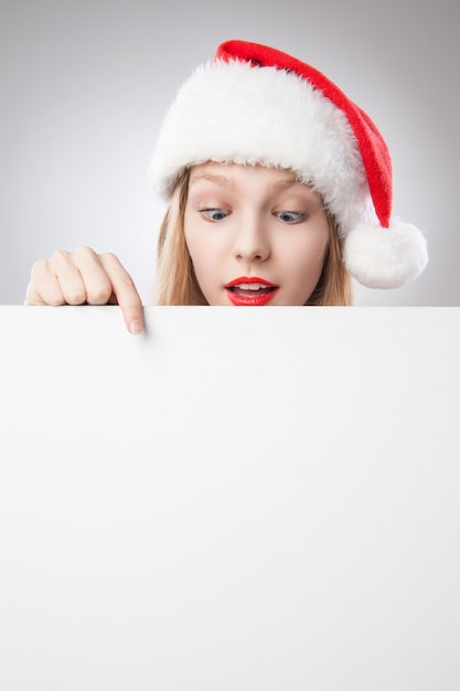 Piękna boże narodzenie kobieta w santa hat wskazując pustą deskę, na białym tle